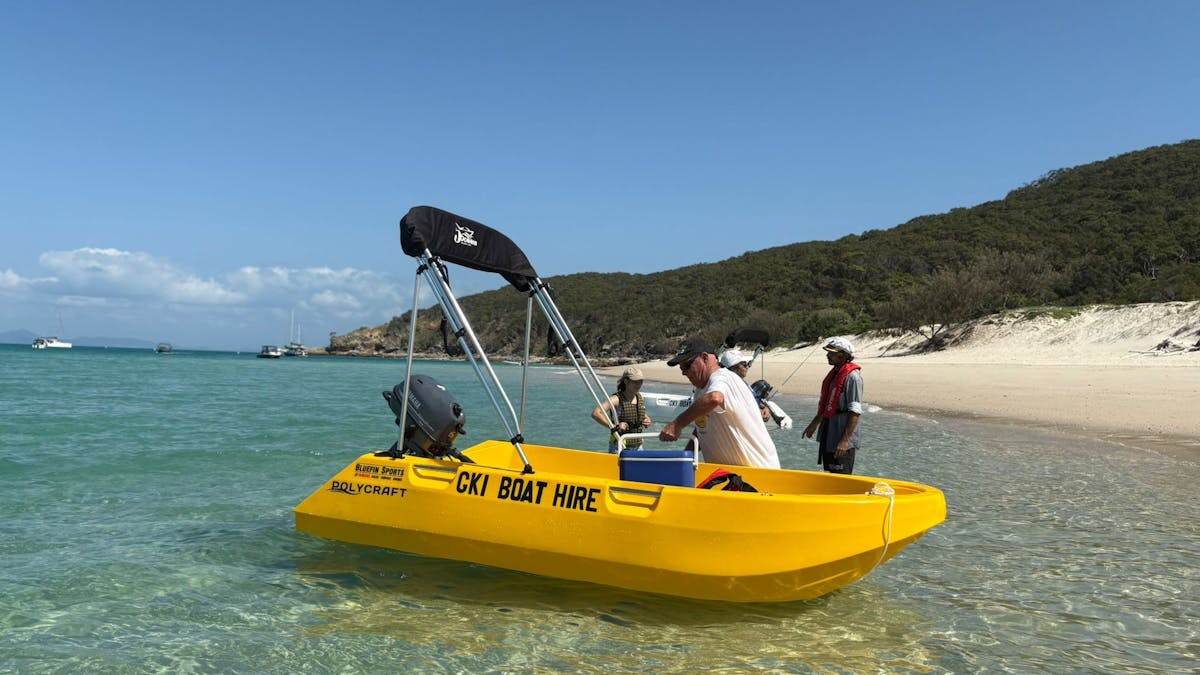 A yellow 3m Polycraft hire boat beached on the shoreline of Great Keppel Island as guests load gear