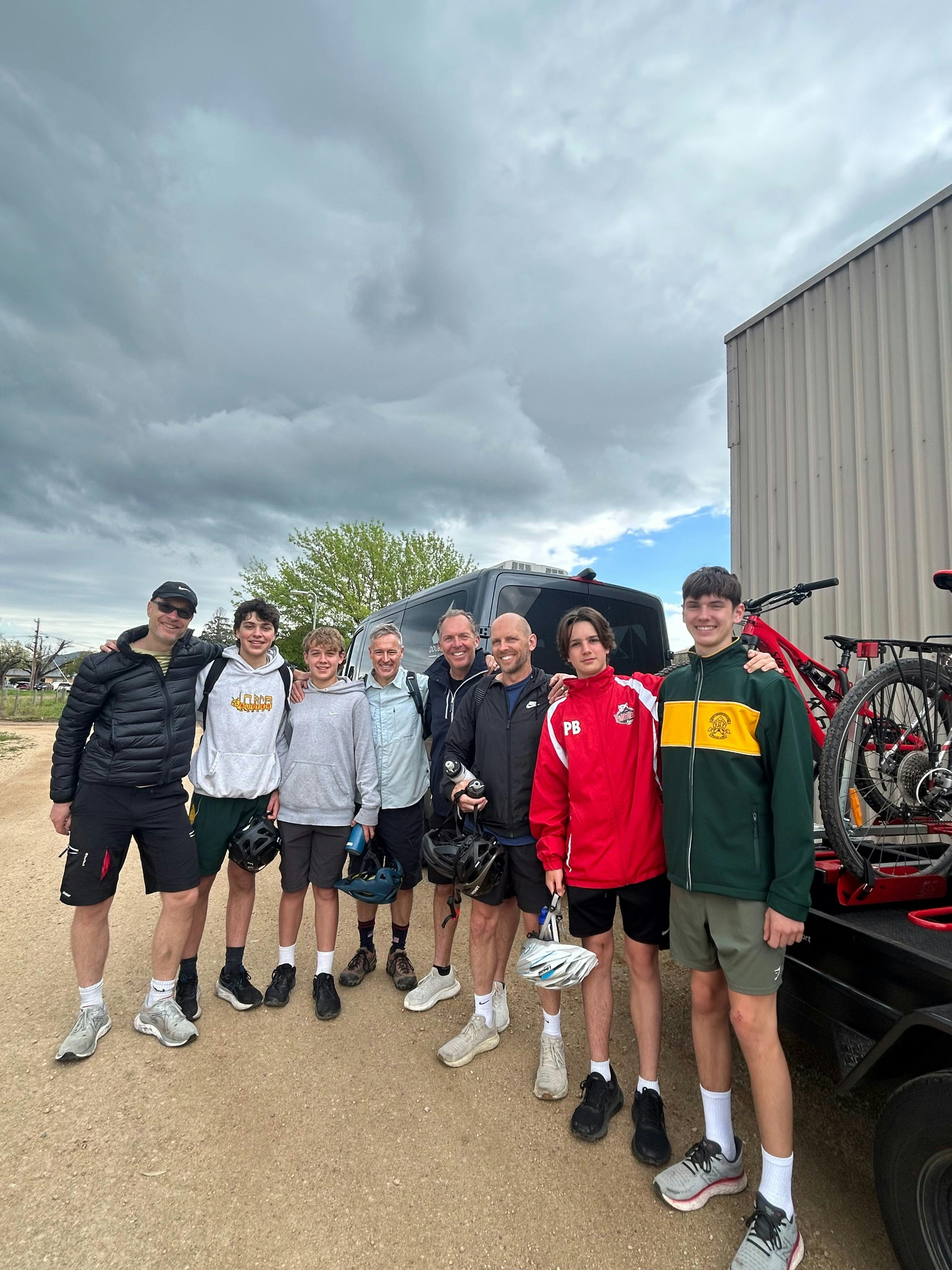 Smiling guests standing beside the Double Black Alpine bike trailer, each with their bikes