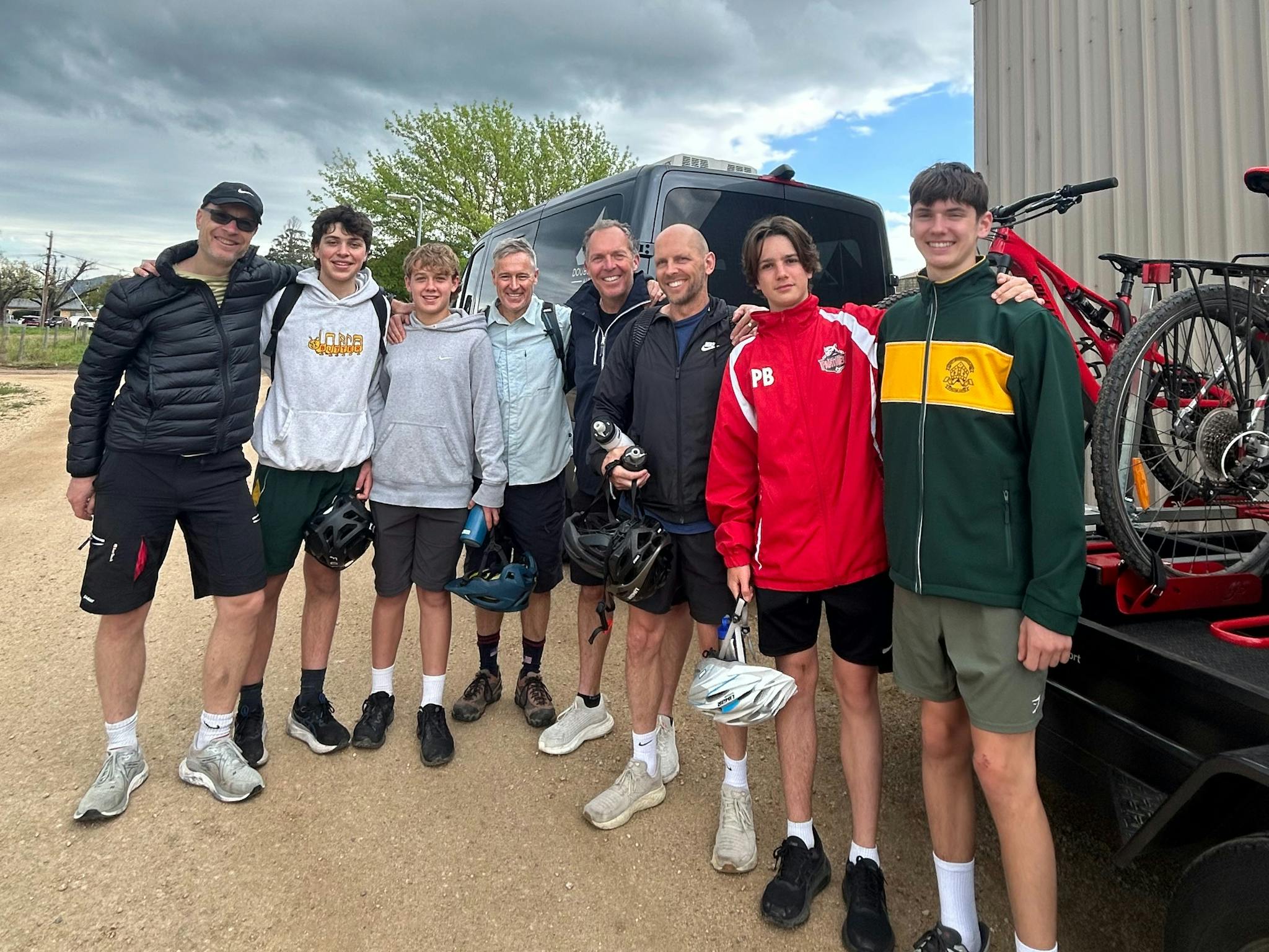 Smiling guests standing beside the Double Black Alpine bike trailer, each with their bikes