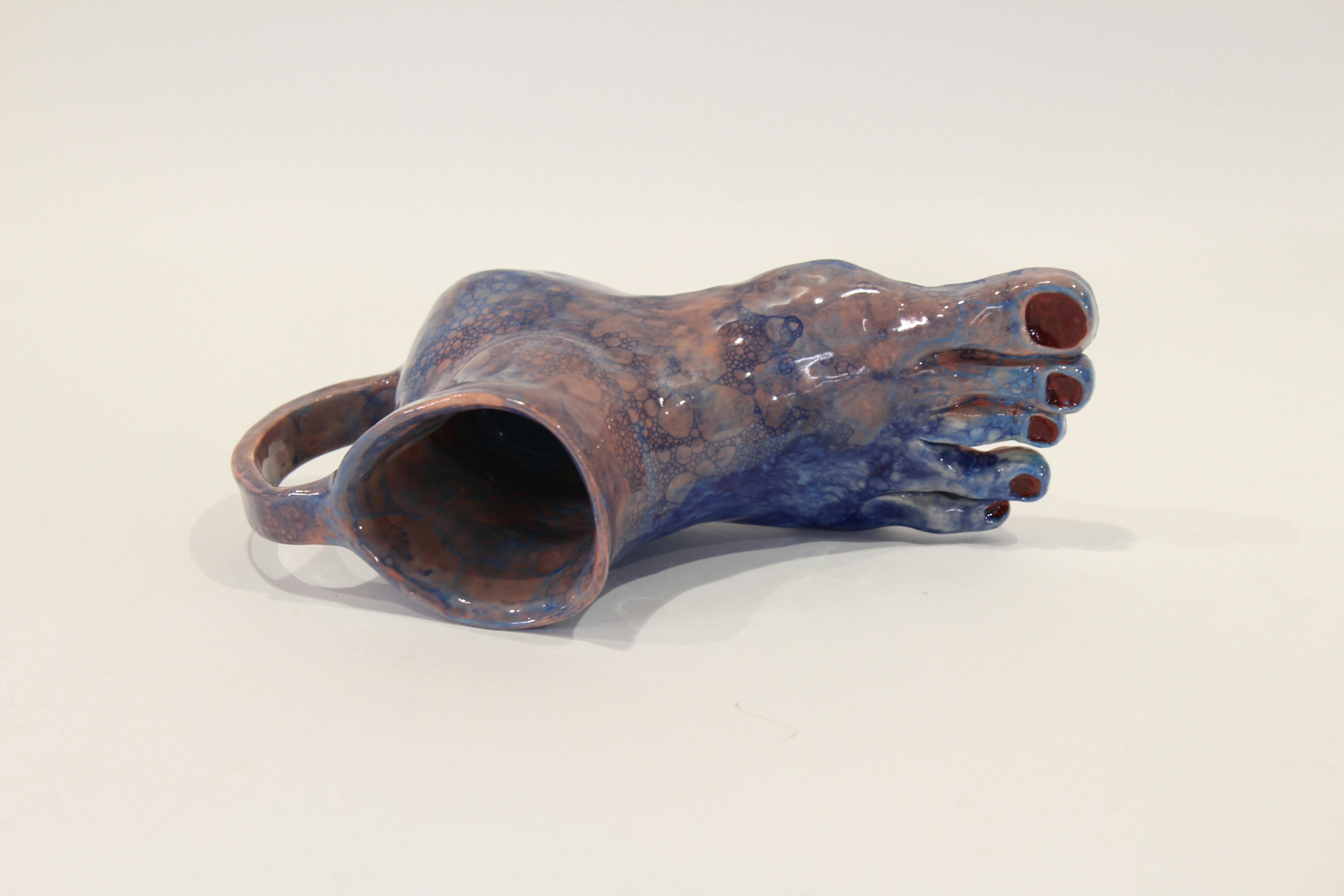 Pottery of a mug that features a human foot as the base of the mug.