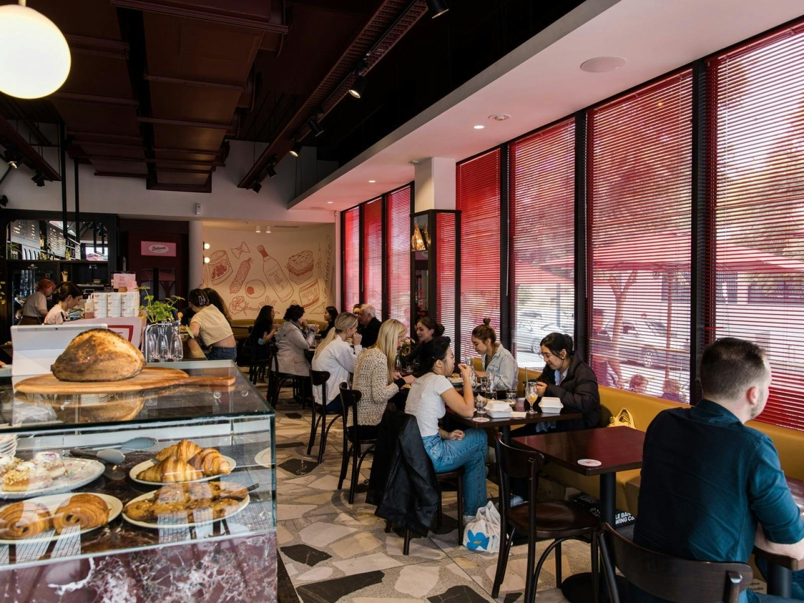 patrons sitting on chairs in the distance and up close is a glass cabinet full of pastries