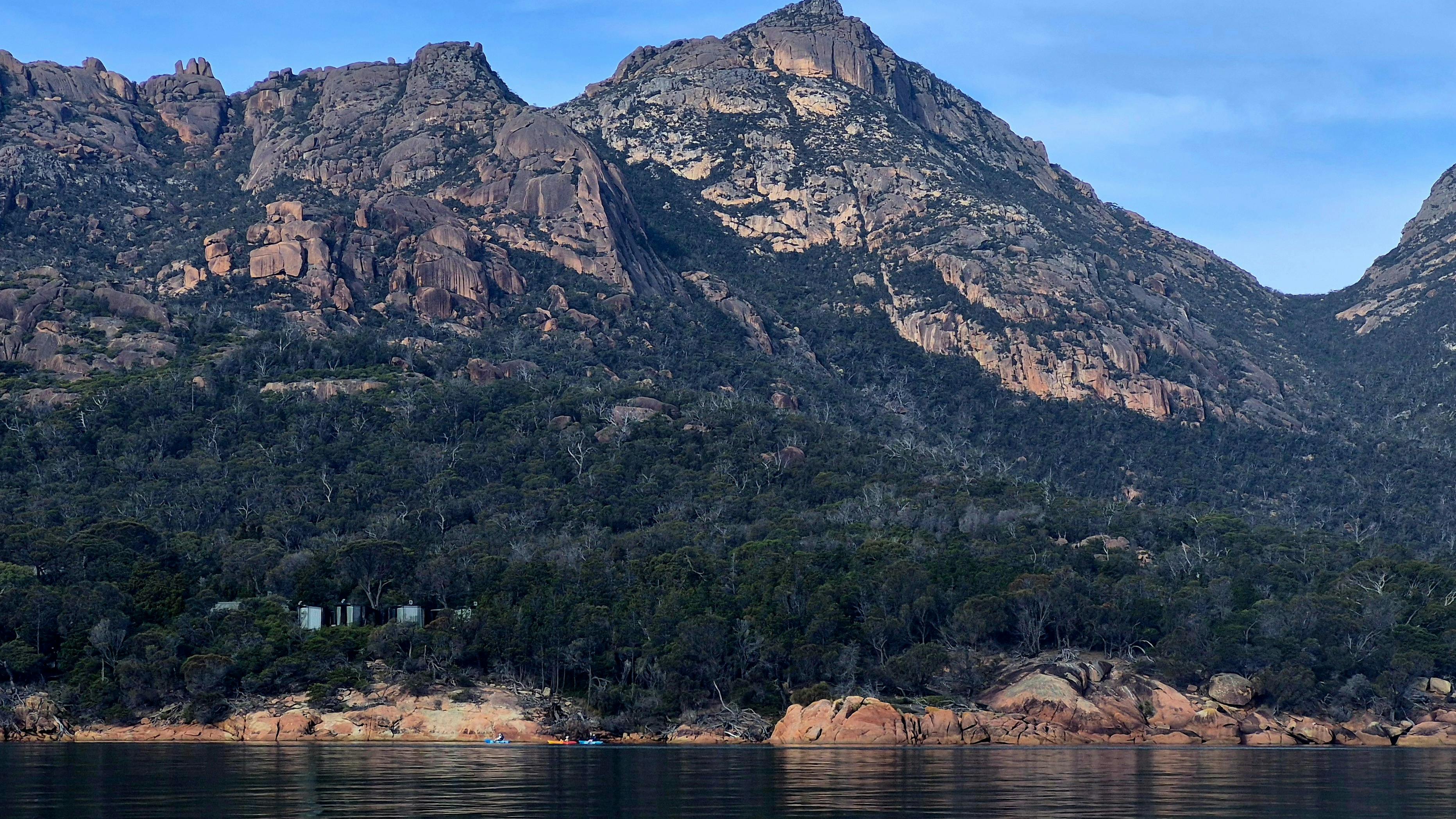 People kayaking on glassy, calm conditions in  Coles Bay in Tasmania, against the scenic Hazards.