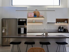 Modern open-plan kitchen with large island bench, bar stools, stainless steel fridge and high ceilin