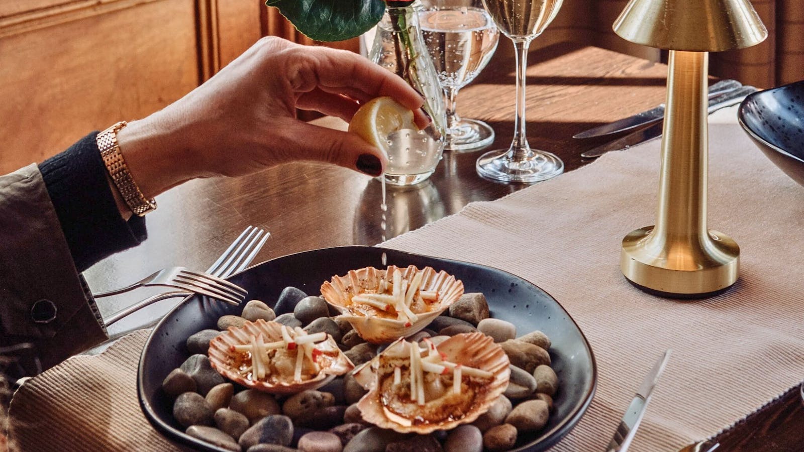 Fresh lemon juice being squeezed over shell roasted scallops, served with a glass of Sparkling Wine