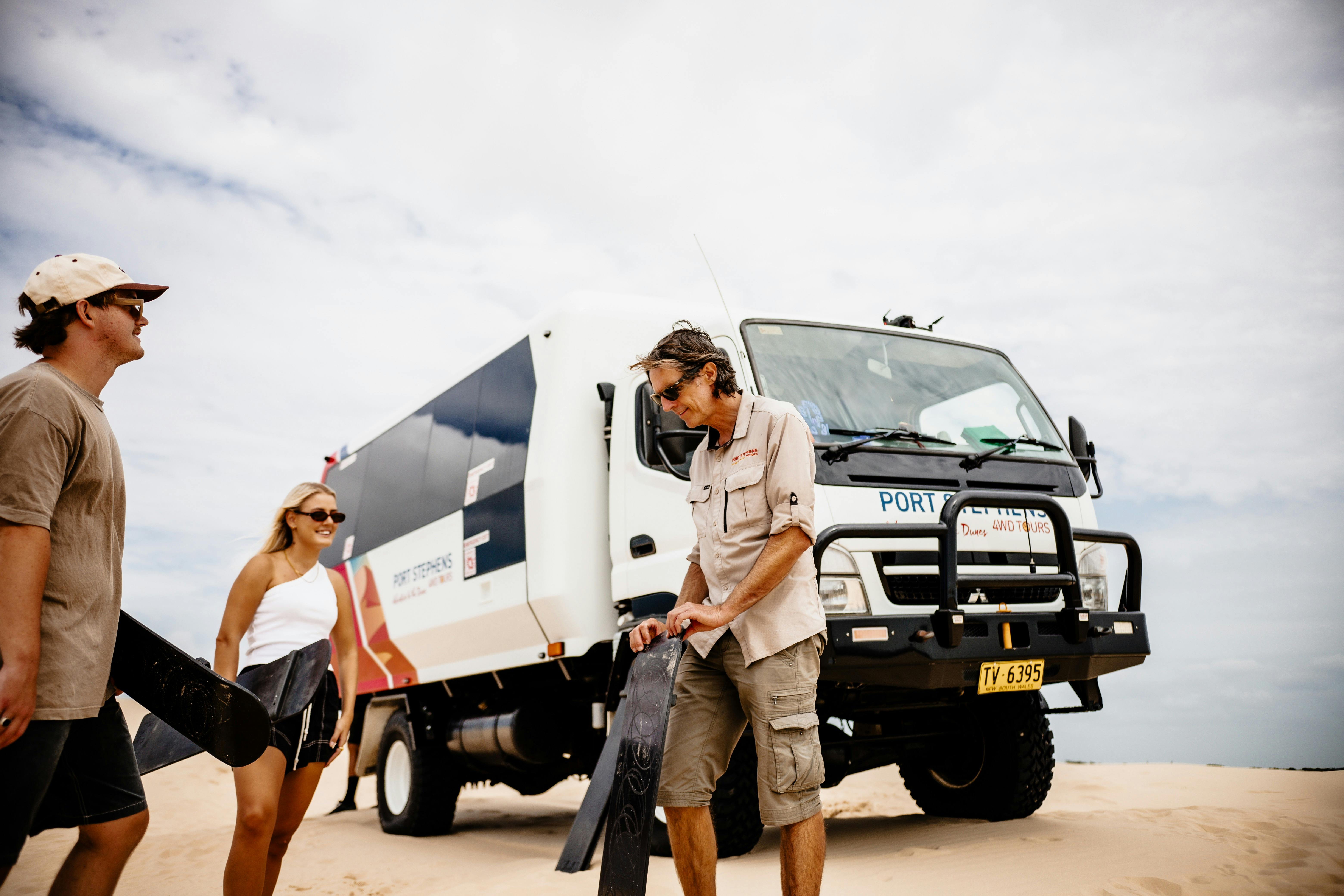 2 adults and a guide standing in front of the bus, the guide is teaching the two people how to board