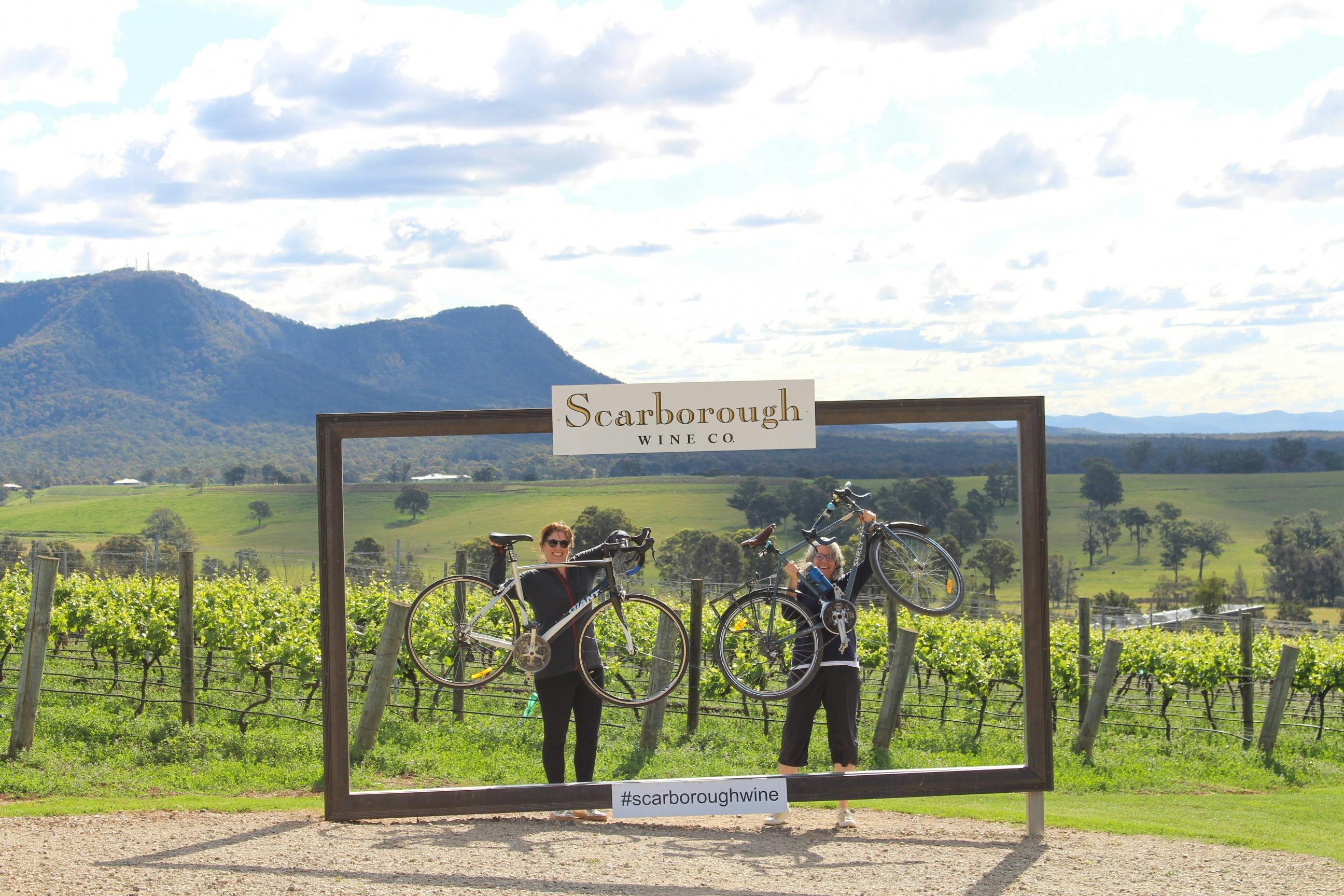 two tour guests at Scarborough wines holding up their bikes triumphantly