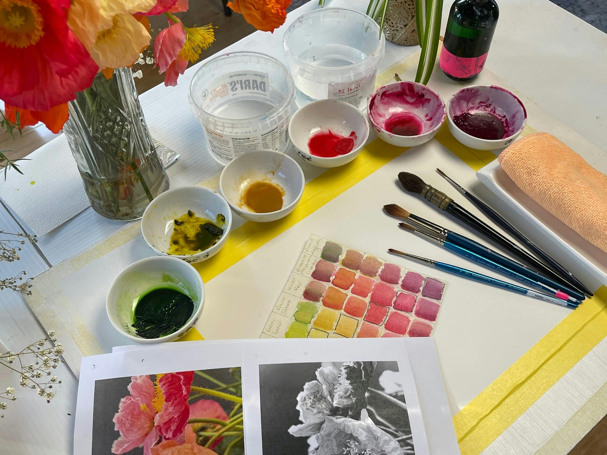 a palette of watercolour paints and a picture of a poppy being painted