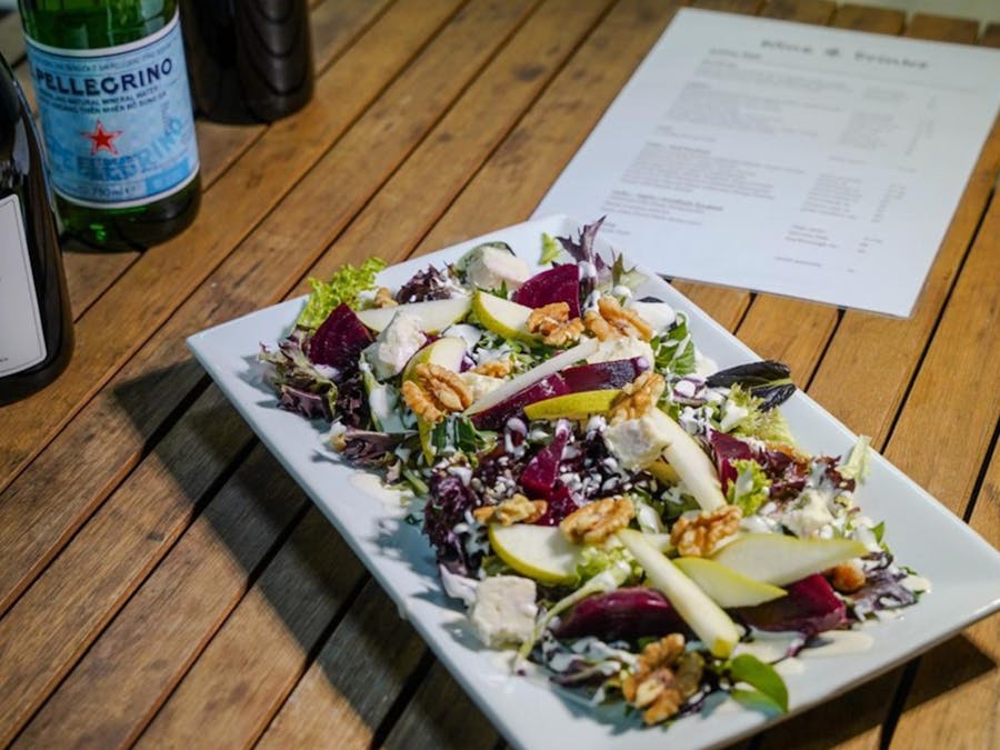 Pear and beetroot salad with gorgonzola, walnuts, and salad leaves on a white rectangle plate