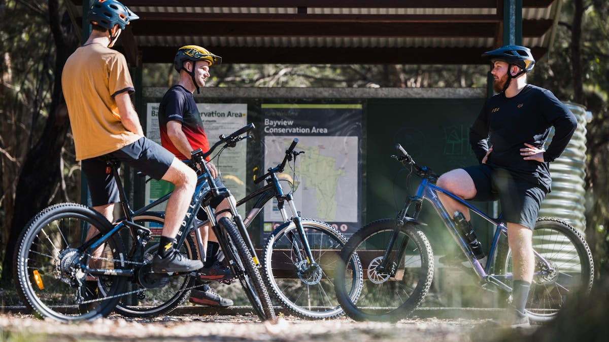Three mountain bike riders stopping near Bayview Conservation Area signage, Redlands Coast