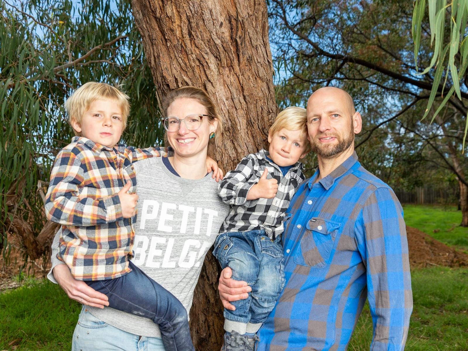 A happy family (mum, dad and 2 young sons) stands in front of gum trees