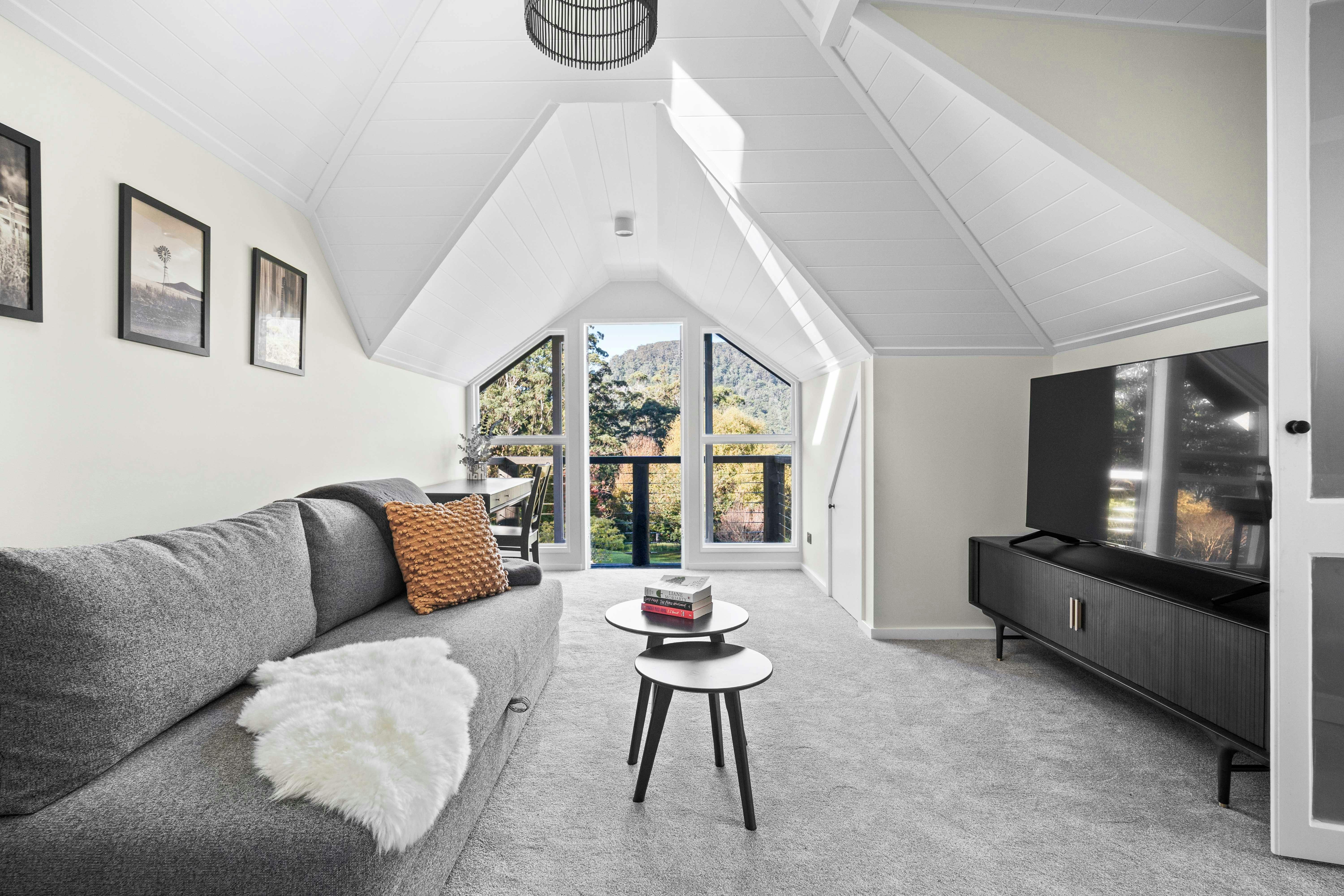 An image of a lounge room with interesting peaked ceiling, TV, sofa and french doors