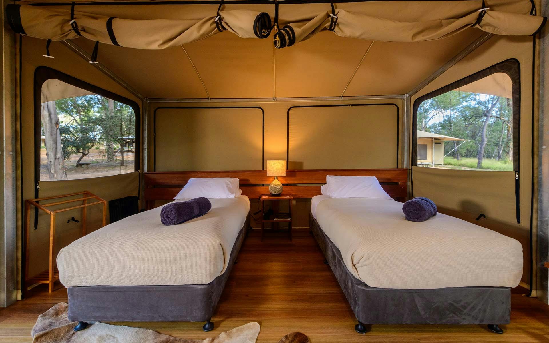 A large tent setup with twin beds, a lamp, wood flooring, and a rolled-up tent flap door
