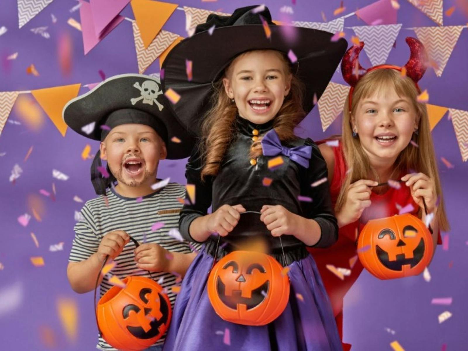 Three children dressed up for Halloween holding pumpkin candy baskets