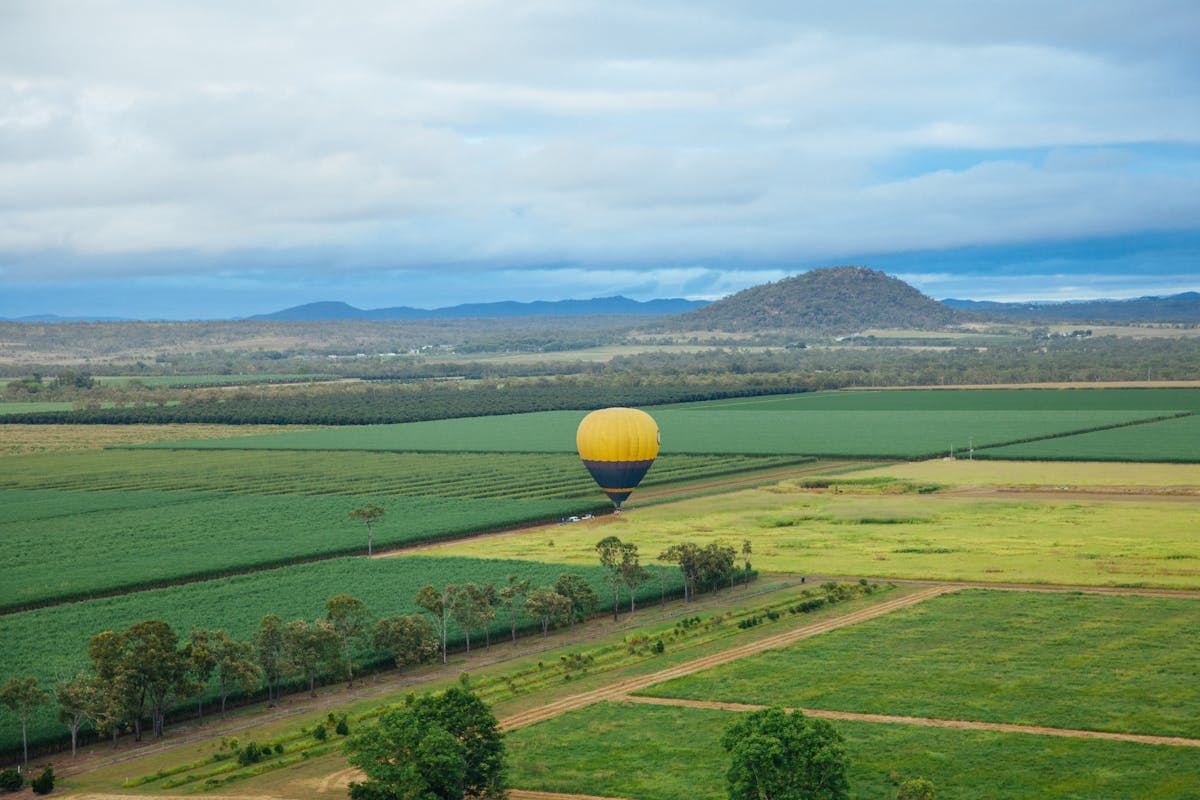 A blue and yellow hot air balloon soars over farm land in Mareeba, Tropical North Queensland.