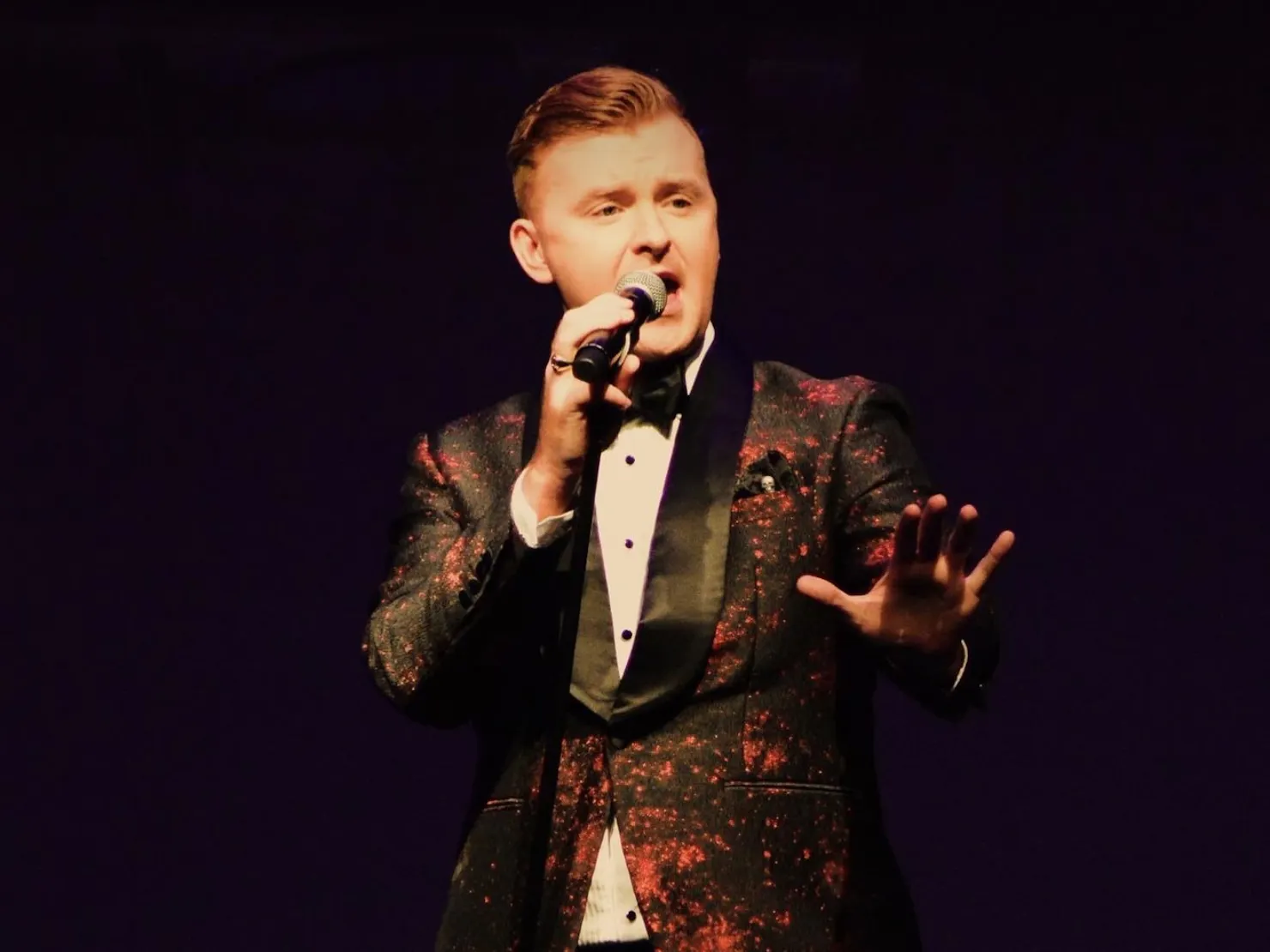 A man in suit singing on stage.