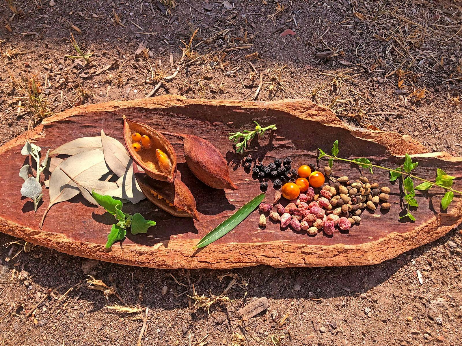 A selection of leaves, nuts and berries are displayed on a traditional wooden vessel