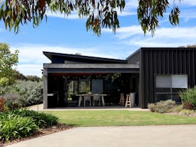Modern black-clad exterior of Harolds on the Hill framed by gardens and mature gum trees in Robe