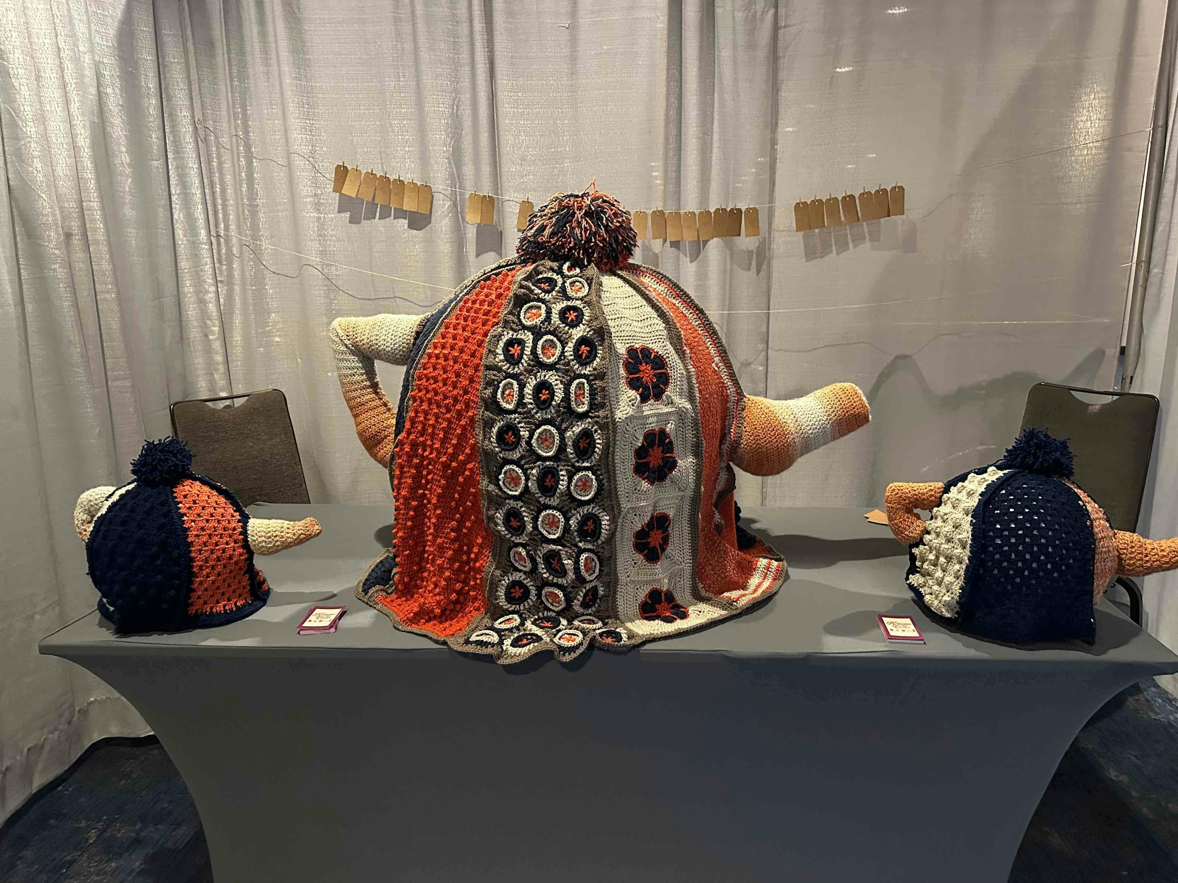 Oversized crochet teapot sitting on atable flanked by 2 smaller crochet teapots