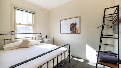 Room with king bed and sink beside it. Photo of a bull on wall as well as clothing rack.