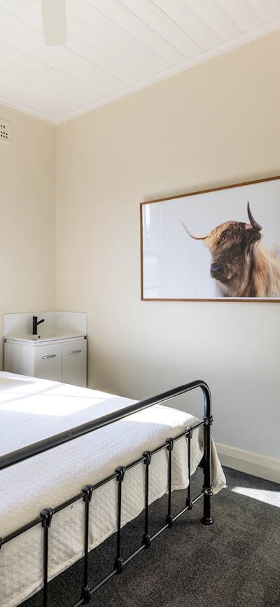 Room with king bed and sink beside it. Photo of a bull on wall as well as clothing rack.