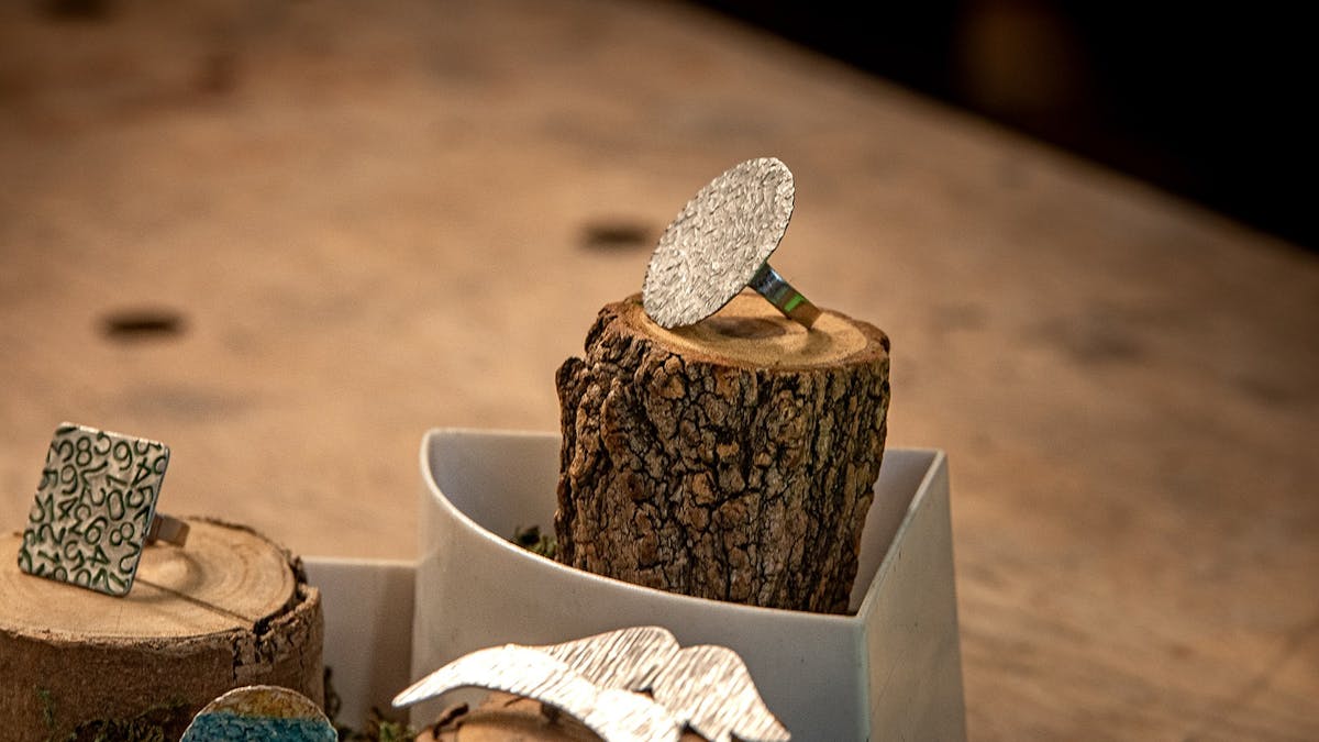 4 handforged rings of different colours, sizes and styles displayed on natural wood stands.