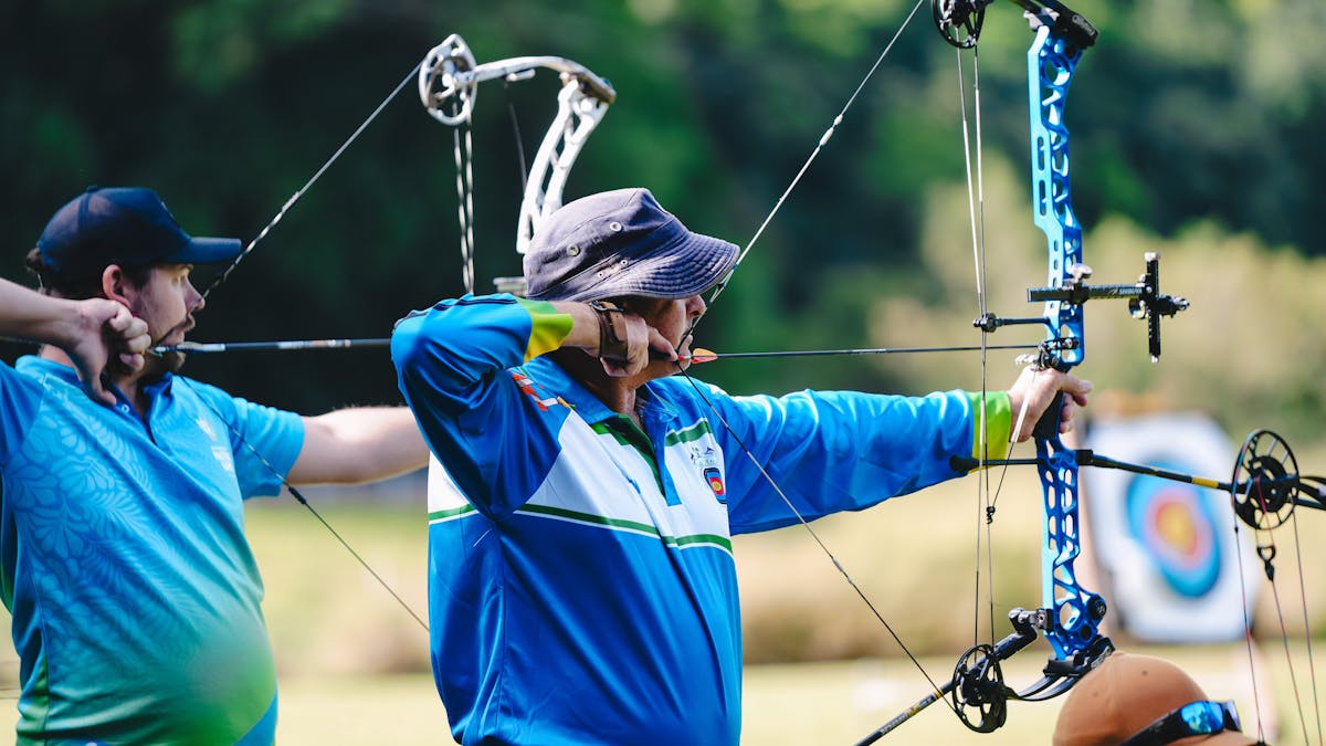 Two archers focus  while drawing their bows at an outdoor shooting range