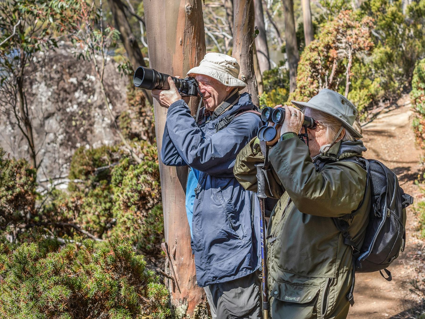 a bird photographer taking a photo of a bird and birder with binoculars lifted to her eyes