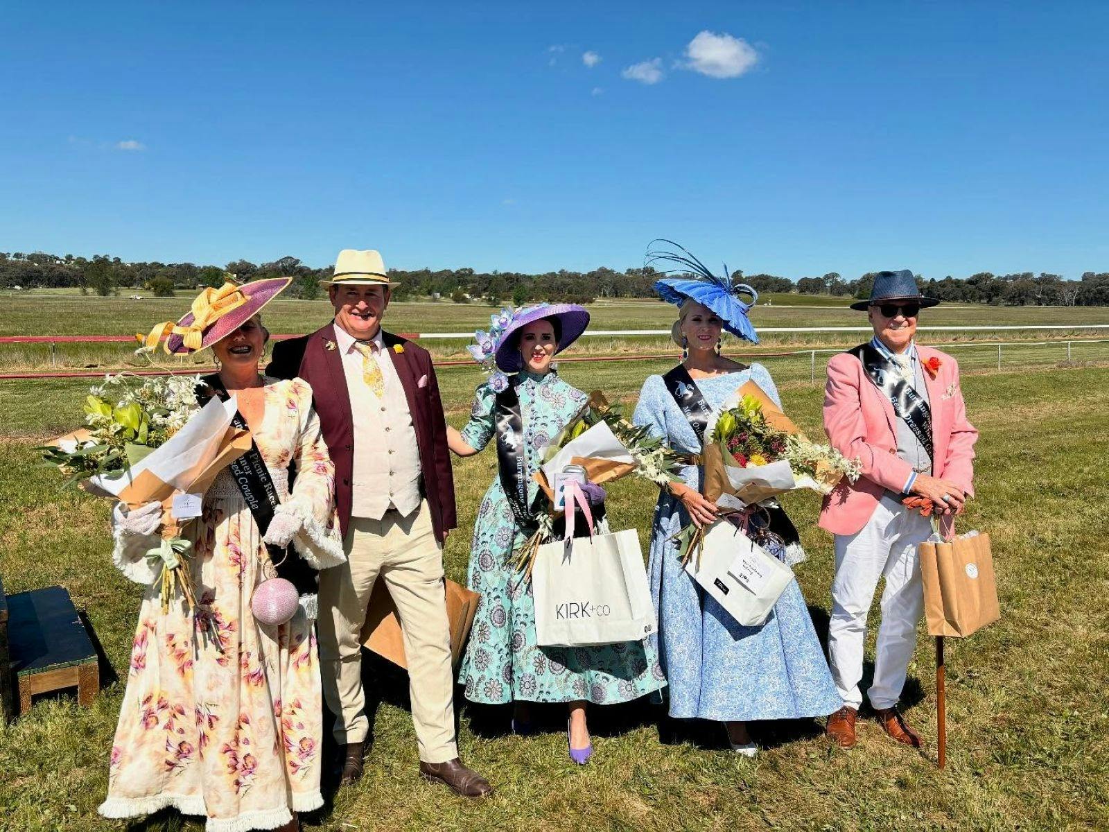 A group of people dressed up in fancy race-day dress and colourful wide brim hats.