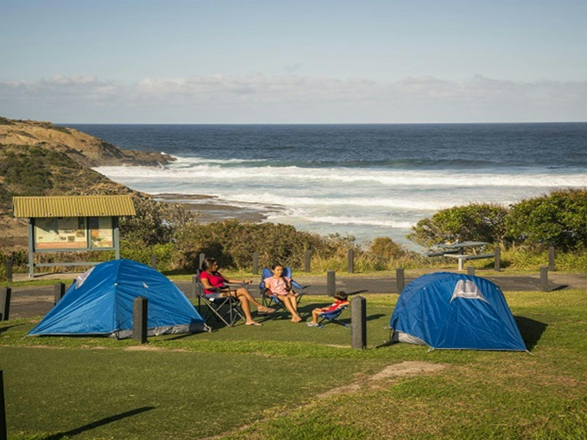 Eine Familie sitzt neben ihren Zelten auf dem Frazer-Campingplatz im Munmorah State Conservation Area. Foto:
