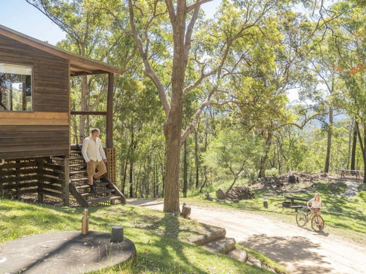A man standing on the stairs of Galong cabins talking to a woman wheeling a bicycle along a path in