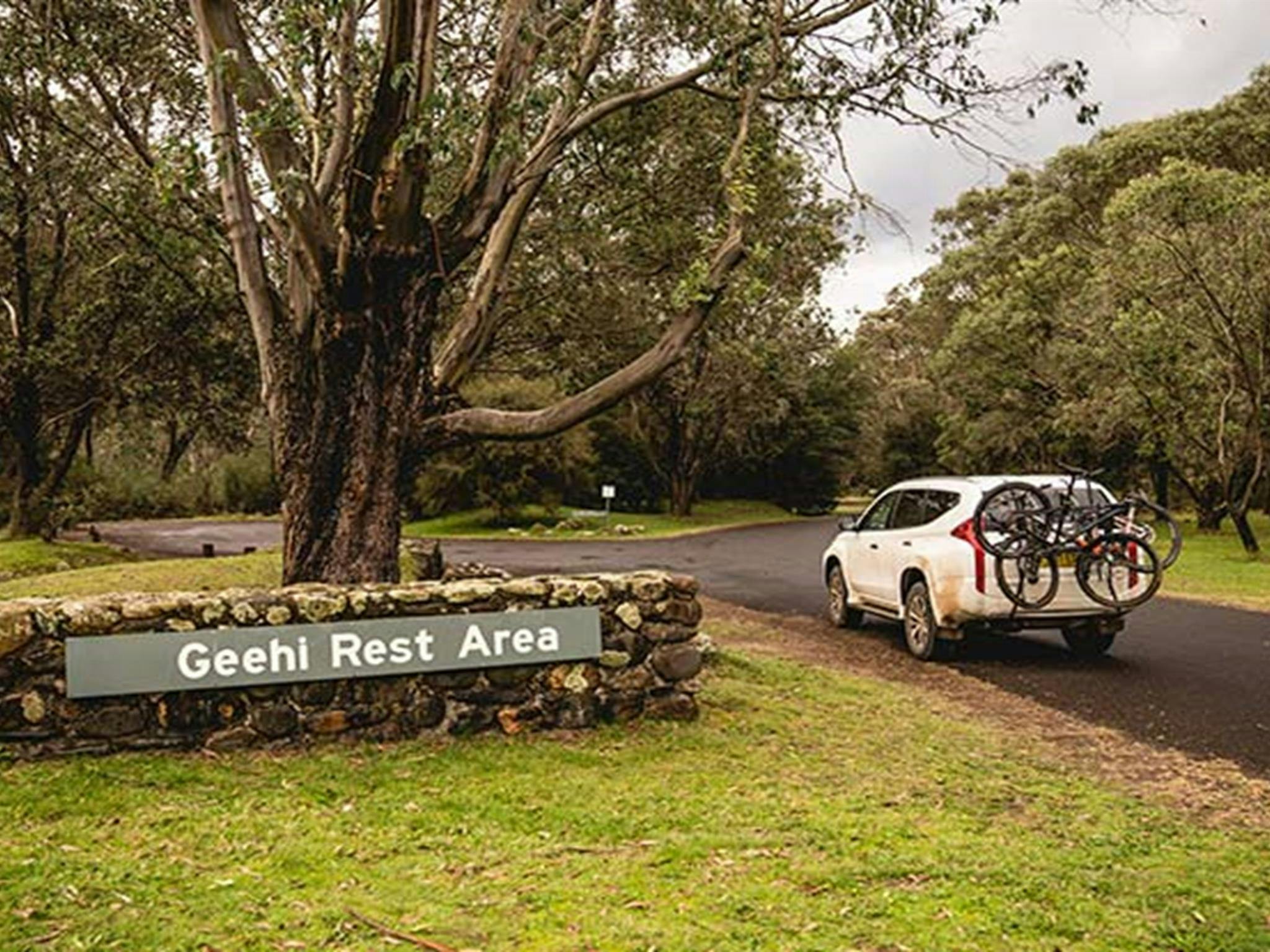 Ein Auto mit Fahrradträger passiert ein Schild am Picknickplatz und Campingplatz Geehi Flats im Kosciuszko-Nationalpark.