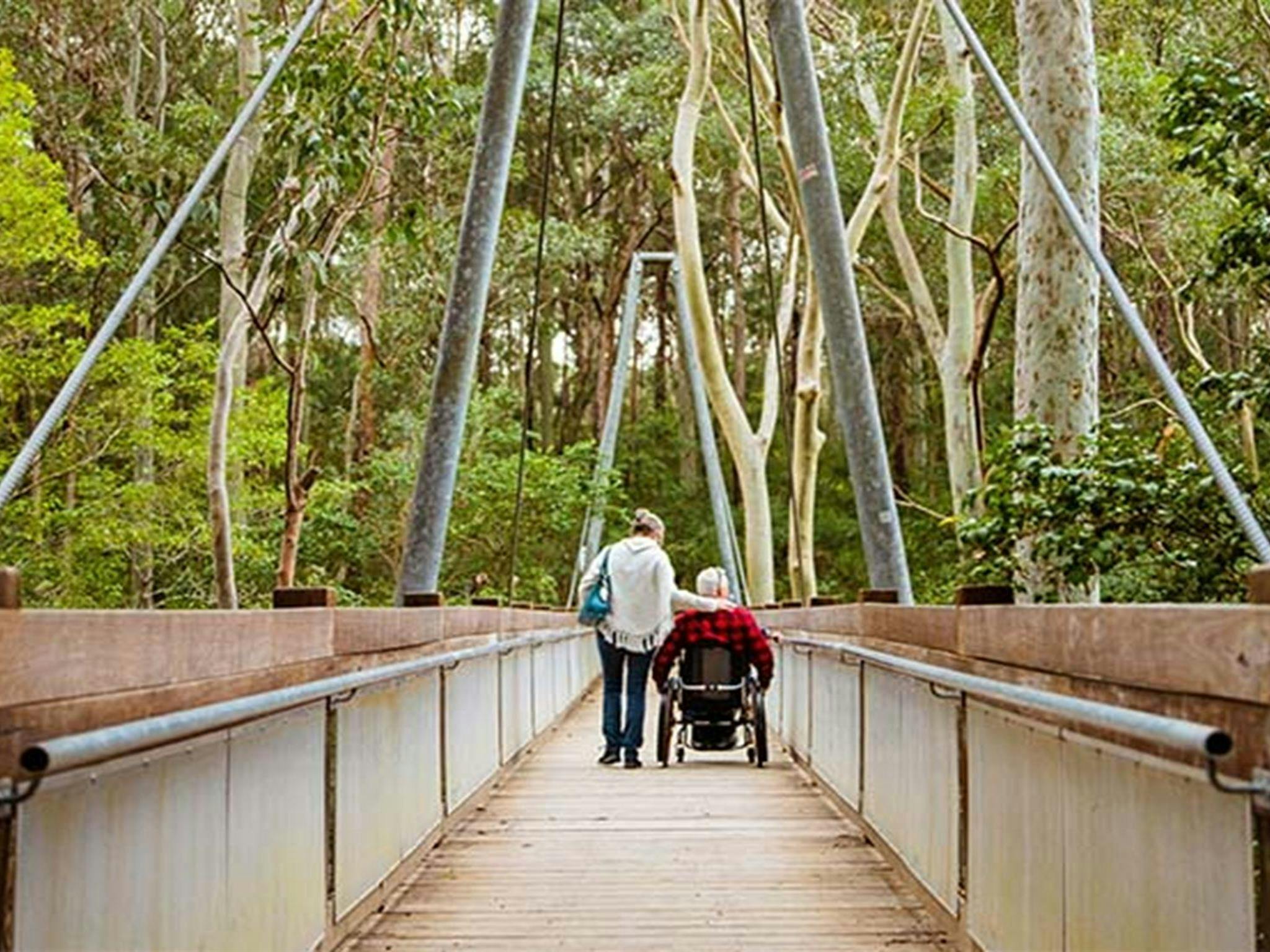 A woman and a man in a wheelchair cross a bridge on Yuelarbah walking track, Glenrock State