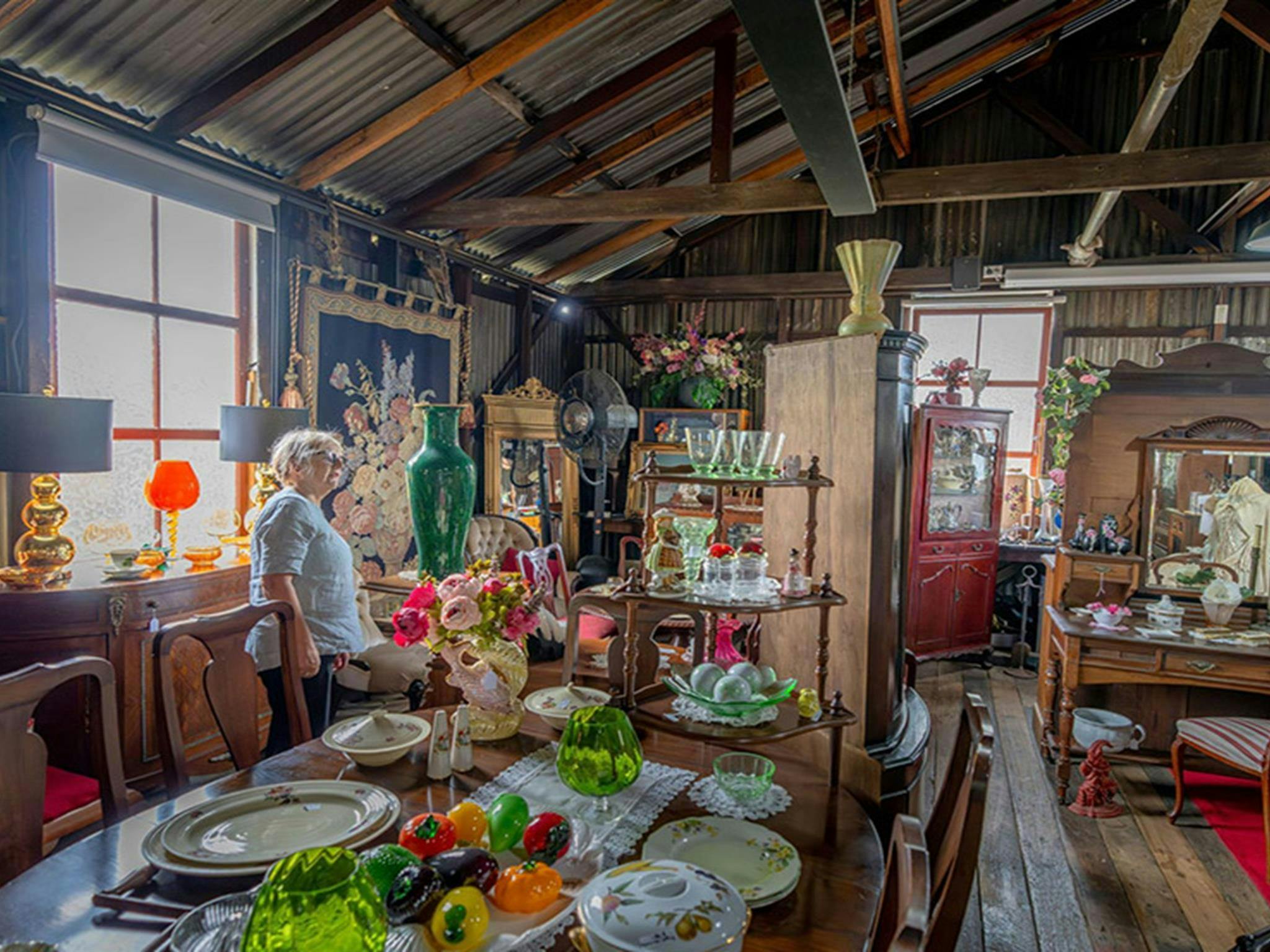 A visitor looking at an antique green vase surrounded by antiques for sale at Gold Rush Antiques