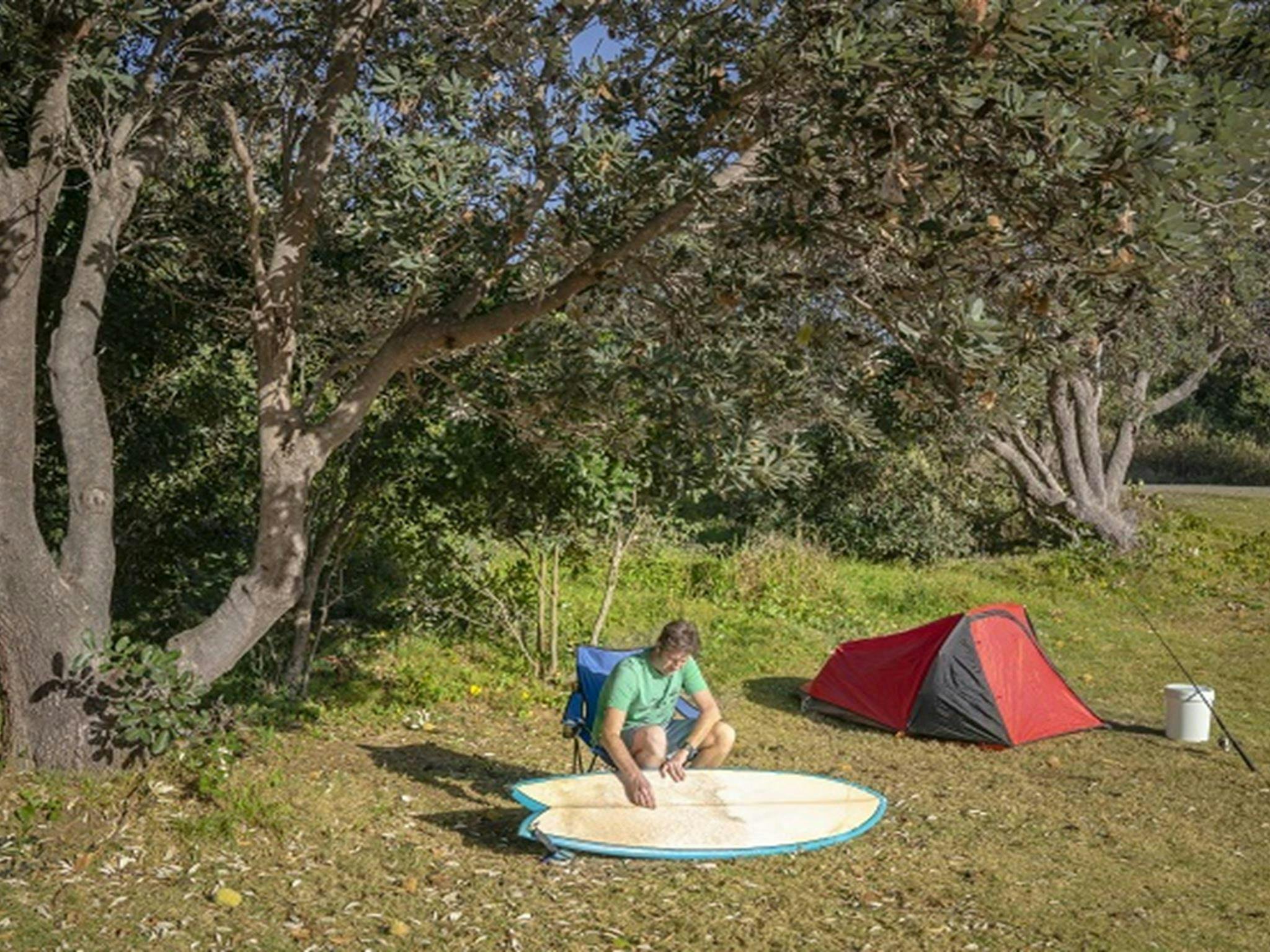 A man cleaning his surf board at Racecourse campground, Goolawah National Park. Photo: John