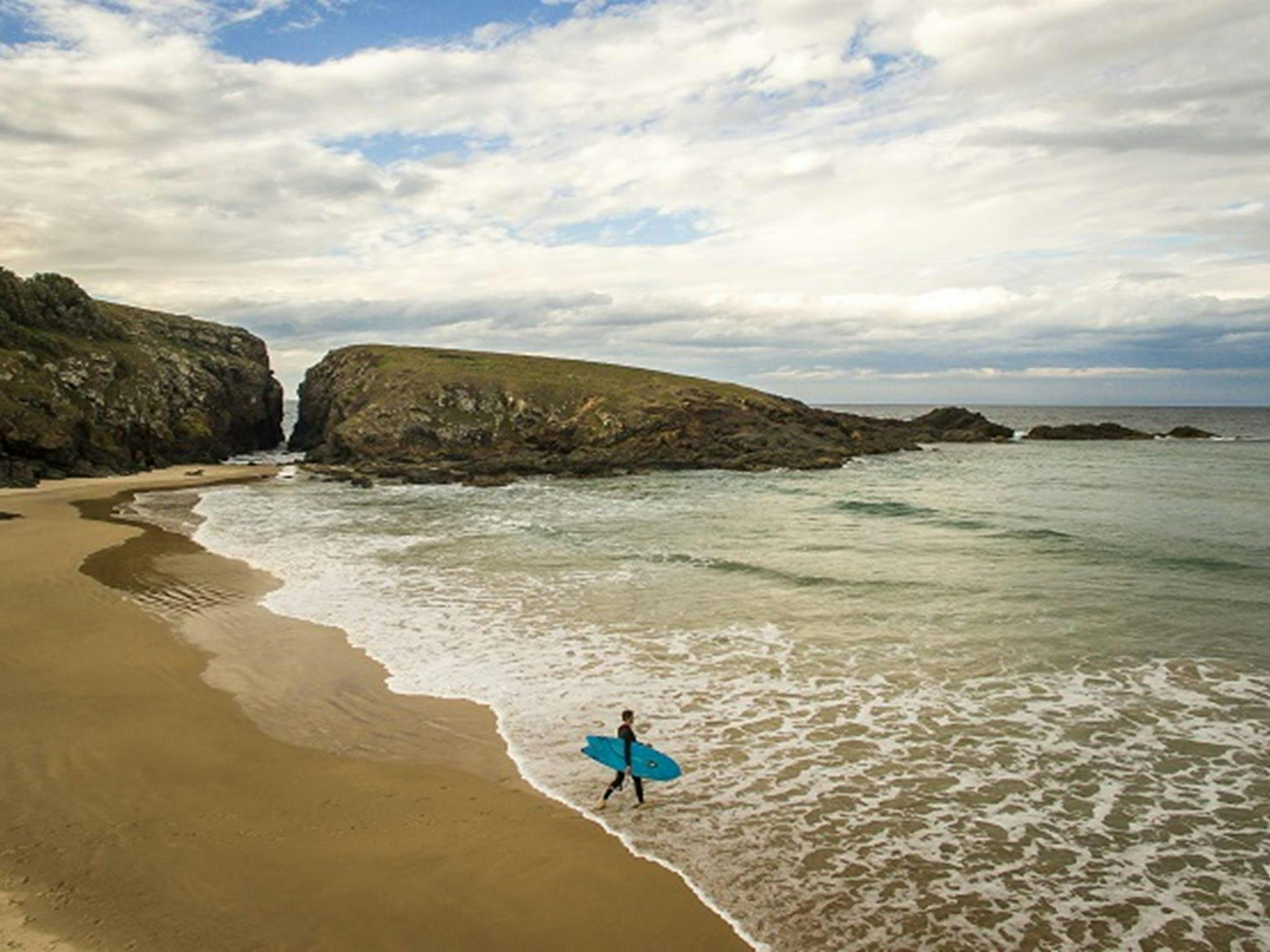 A surfer with his board walking along the beach into the ocean at Goolawah National Park. Photo: