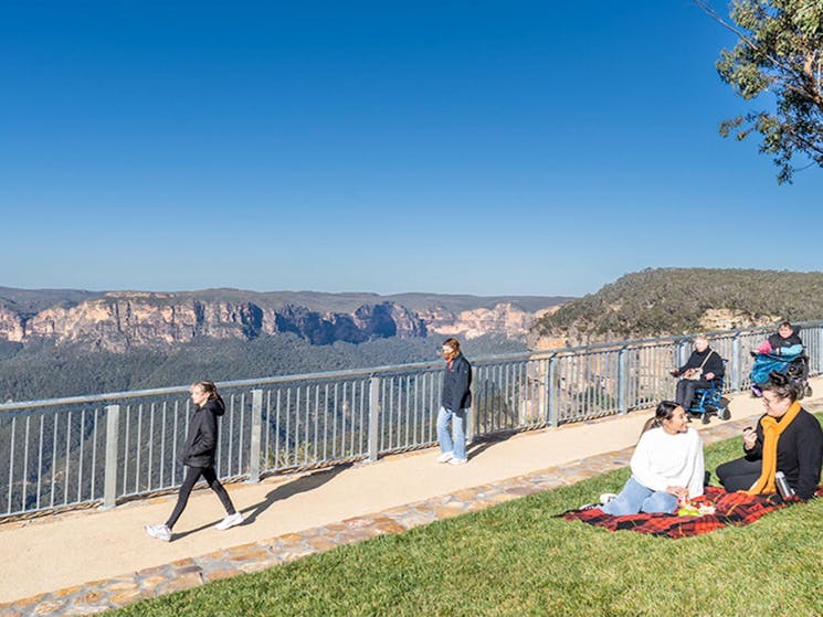Visitors using an accessible path and having a picnic on the grass at Govetts Leap lookout. Credit: