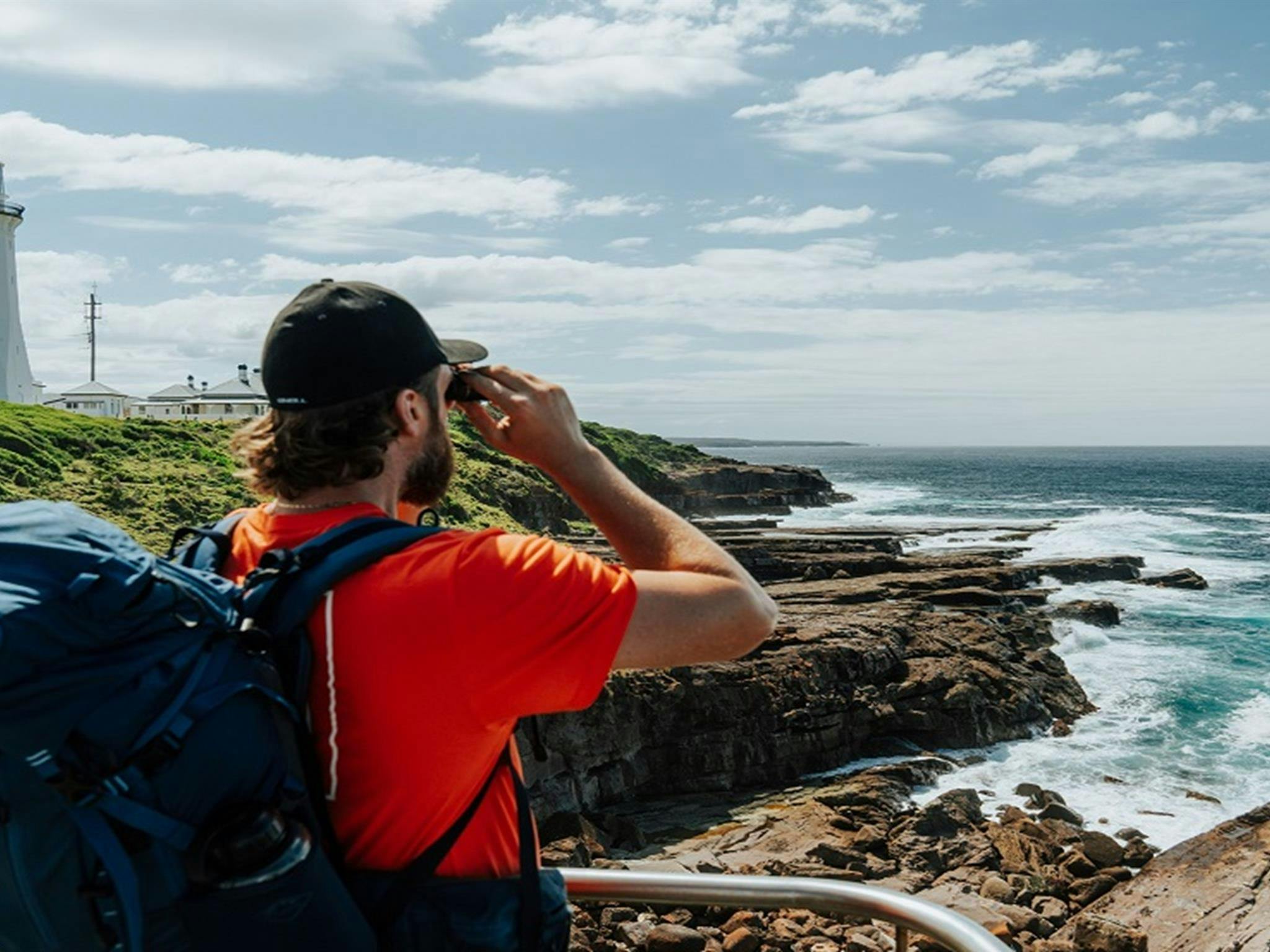 Visitor gazing through a pair of binoculars towards the vast expanse of rugged coastline at Green