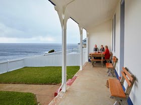 Friends sitting on the verandah with views of the ocean at Green Cape Lightstation Keeper's Cottage.