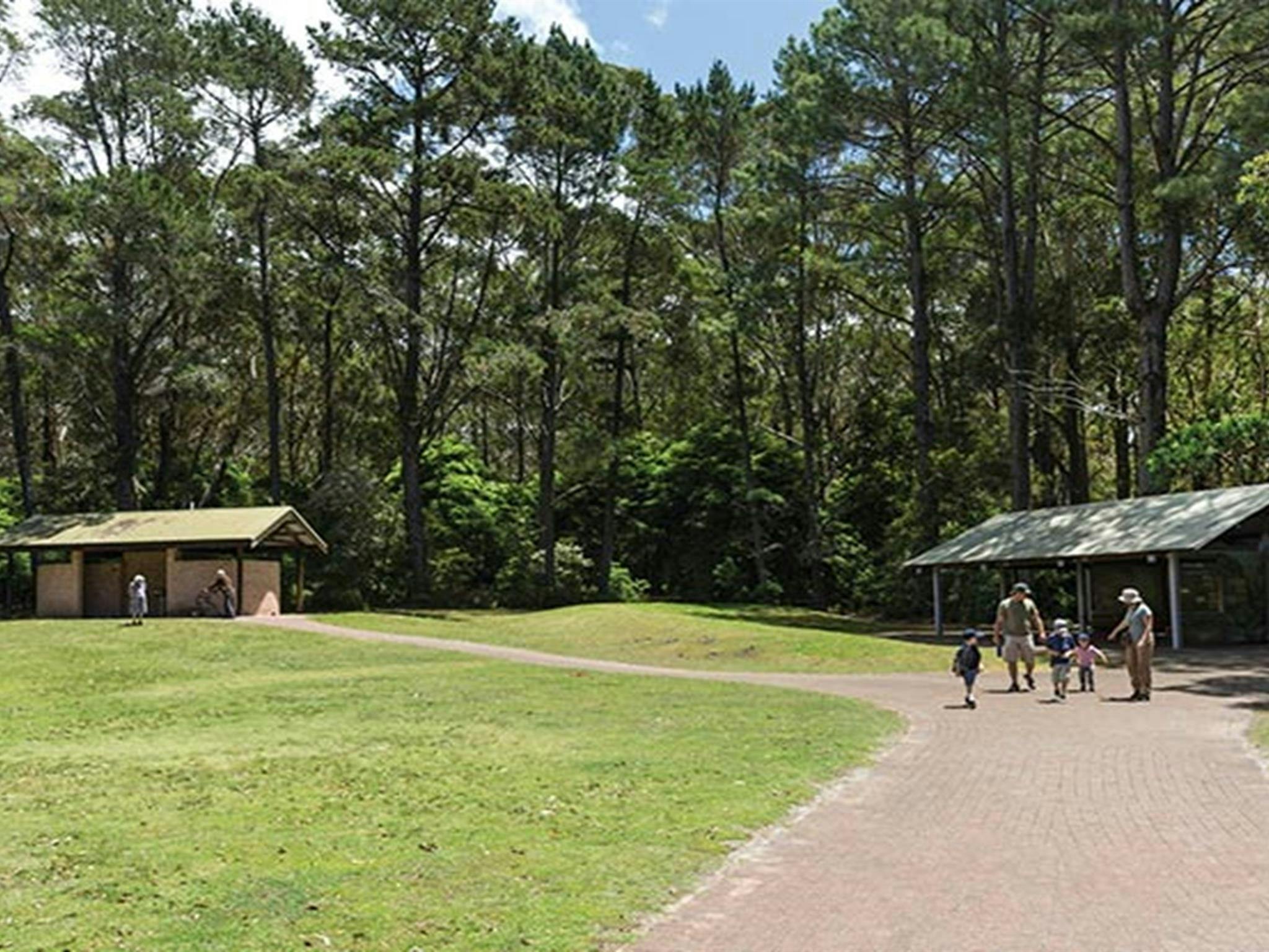 Eine Familie geht an einem Picknickpavillon im Picknickbereich Greenfield Beach im Jervis Bay Nationalpark vorbei. Foto: