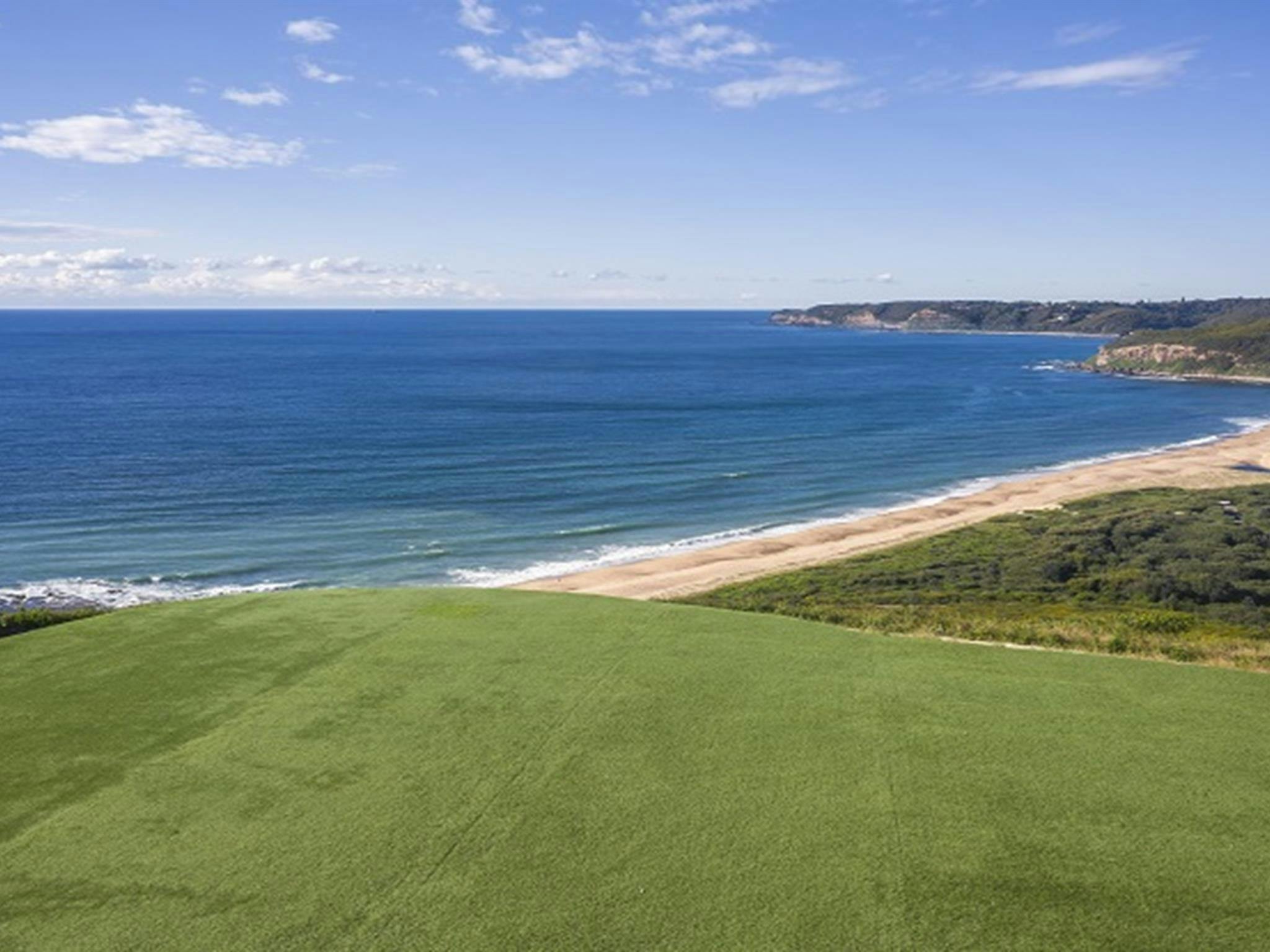 View of the lawn at Hickson Street lookout, with beach,  bushland and ocean in the background.