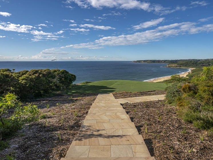 View of paved path leading to the lawn at Hickson Street lookout, with beach,  bushland and ocean in