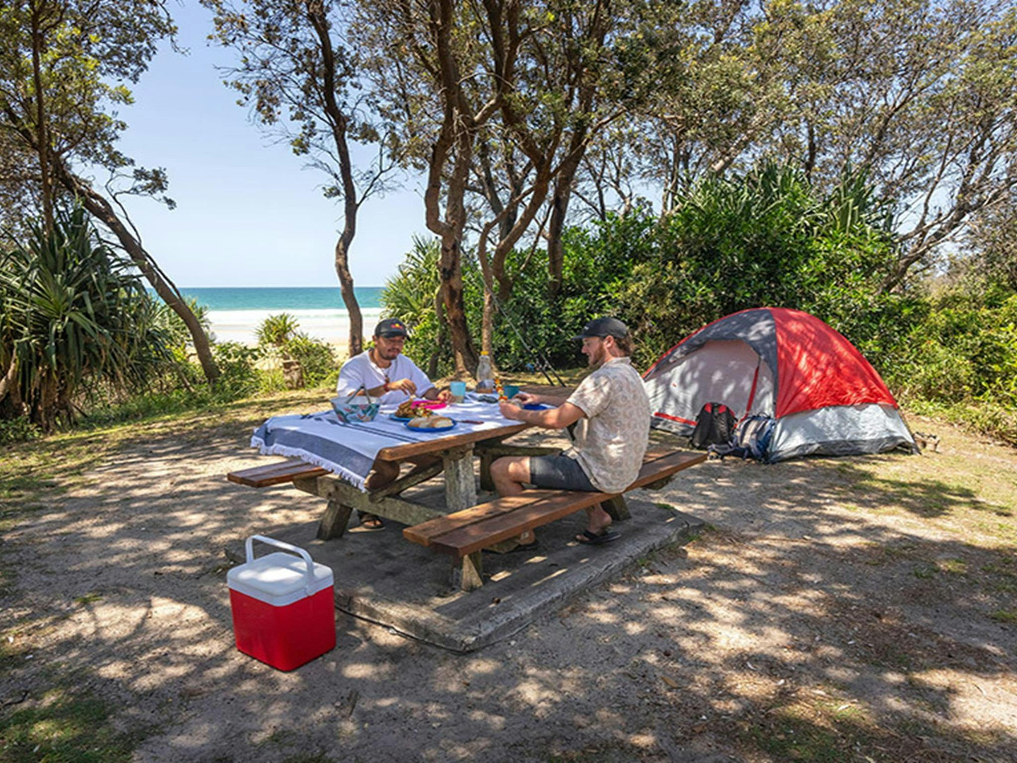 Camper genießen ihr Mittagessen auf der Picknickbank ihres Zeltplatzes auf dem Campingplatz Ilaroo. Foto: John