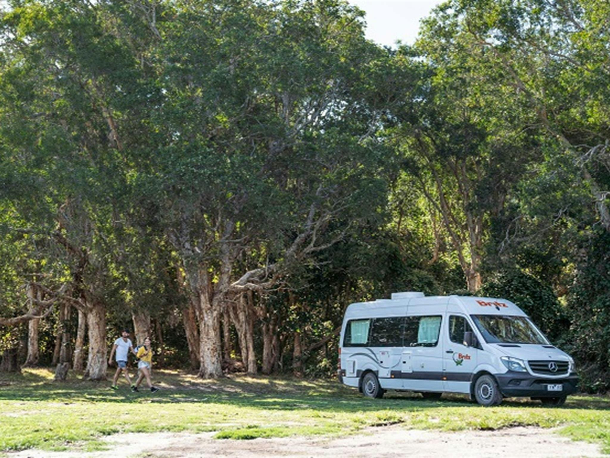 Ein Paar, das über den Campingplatz Kylies Beach zu seinem Wohnmobil im Crowdy Bay Nationalpark spaziert. Foto: