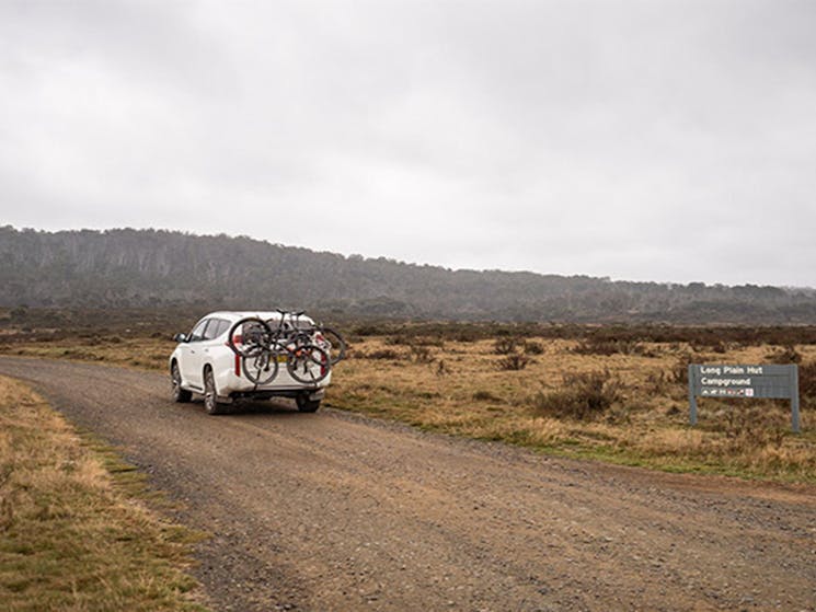A car carrying bikes drives past a sign on an unsealed road, Kosciuszko National Park. Photo: Robert