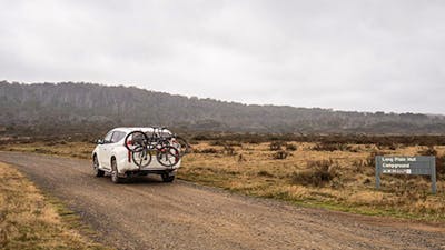 A car carrying bikes drives past a sign on an unsealed road, Kosciuszko National Park. Photo: Robert