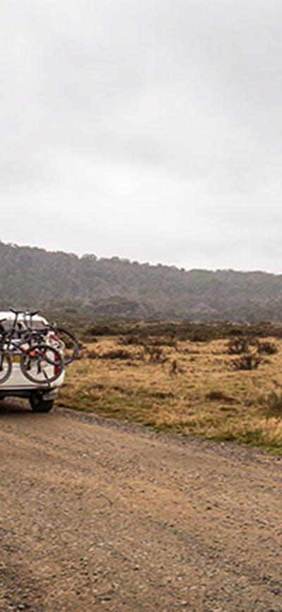 A car carrying bikes drives past a sign on an unsealed road, Kosciuszko National Park. Photo: Robert