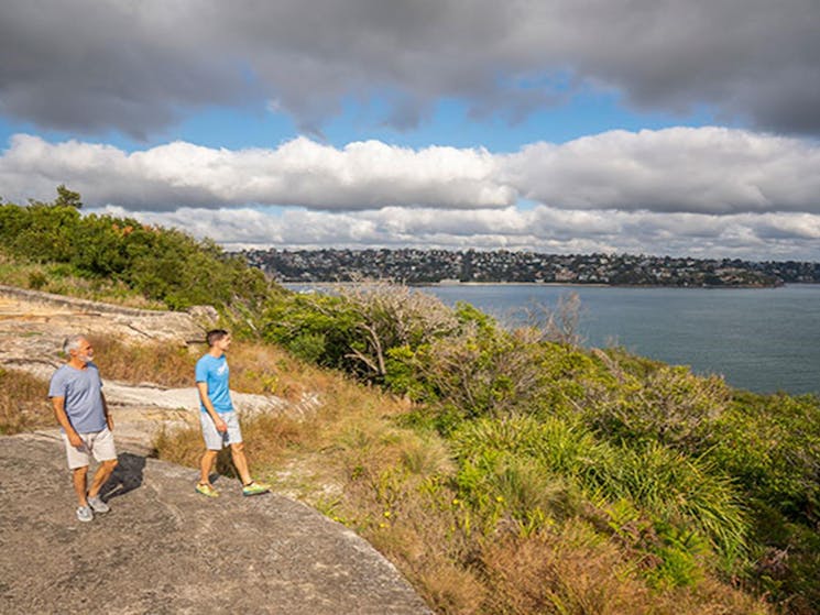 Two people walking along the rocks at Middle Head – Gubbuh Gubbuh in Sydney Harbour National Park.