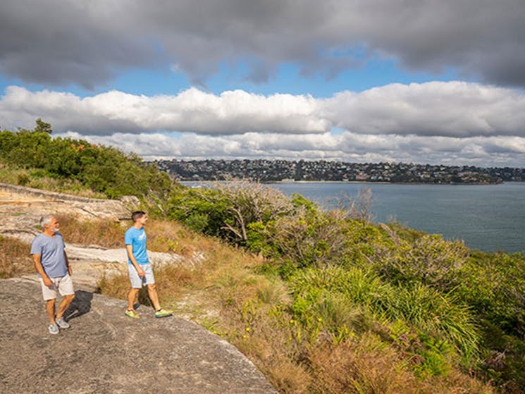 Two people walking along the rocks at Middle Head – Gubbuh Gubbuh in Sydney Harbour National Park.