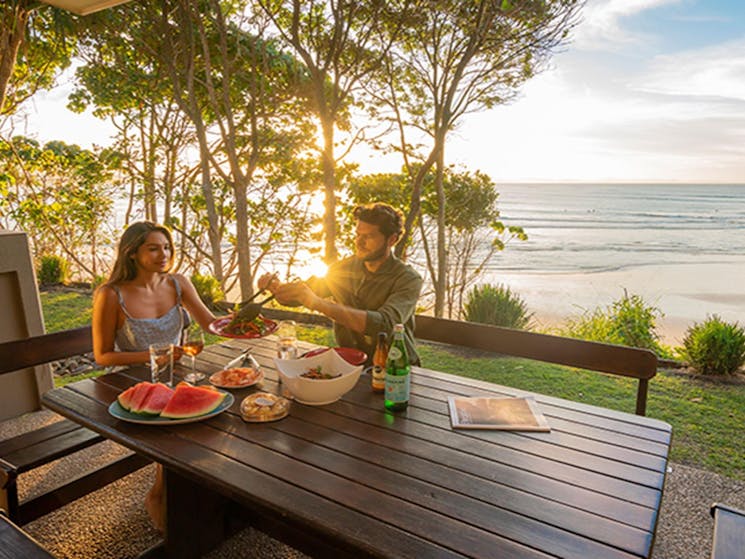 Couple eating outdoors at sunset with views of the beach from Mildenhall Cottage. Photo: John