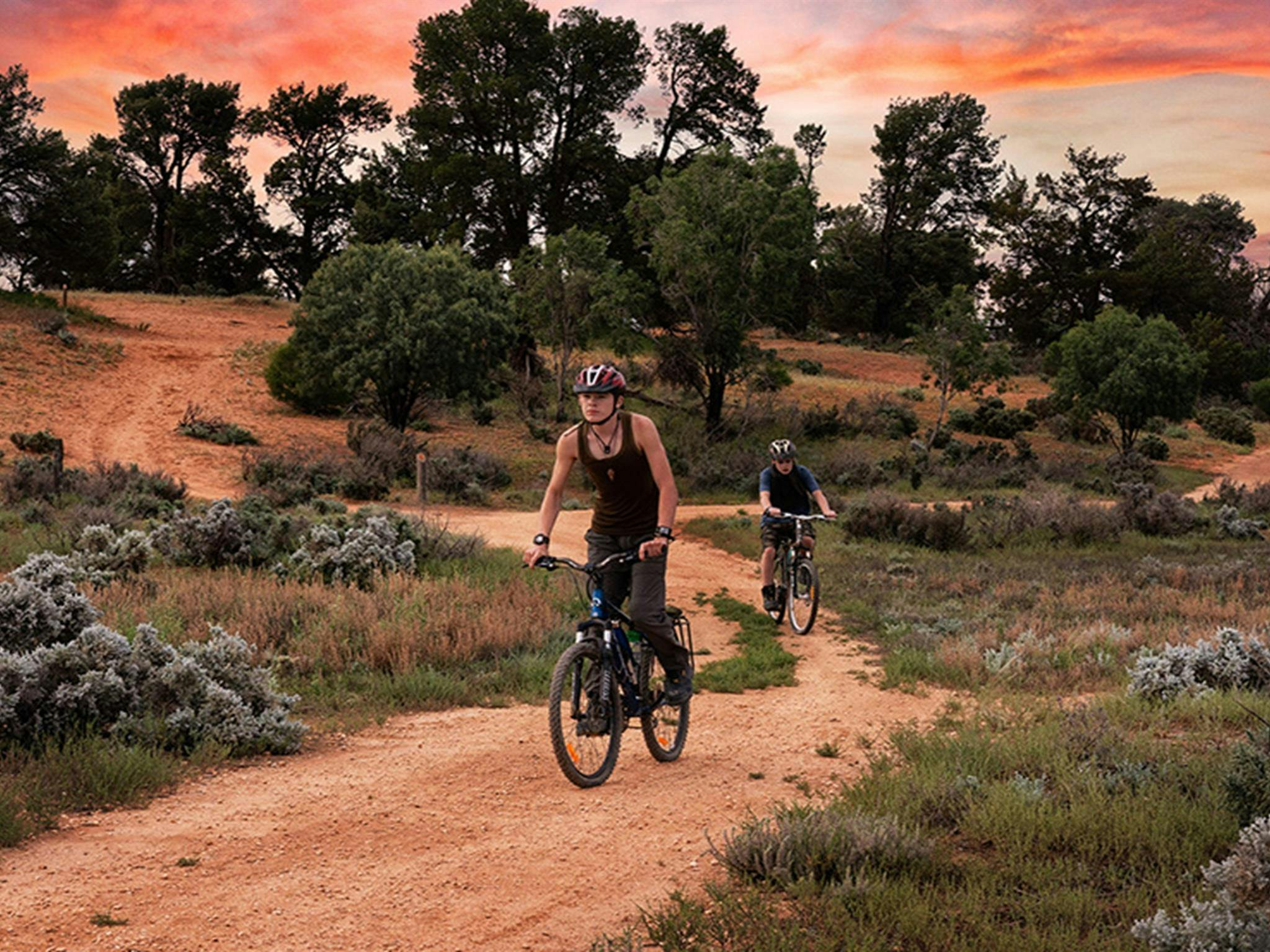 붉은 흙길과 아름다운 분홍빛 석양을 배경으로 문고 호수 사이클링 트랙에서 산악자전거를 타는 두 명의 라이더.